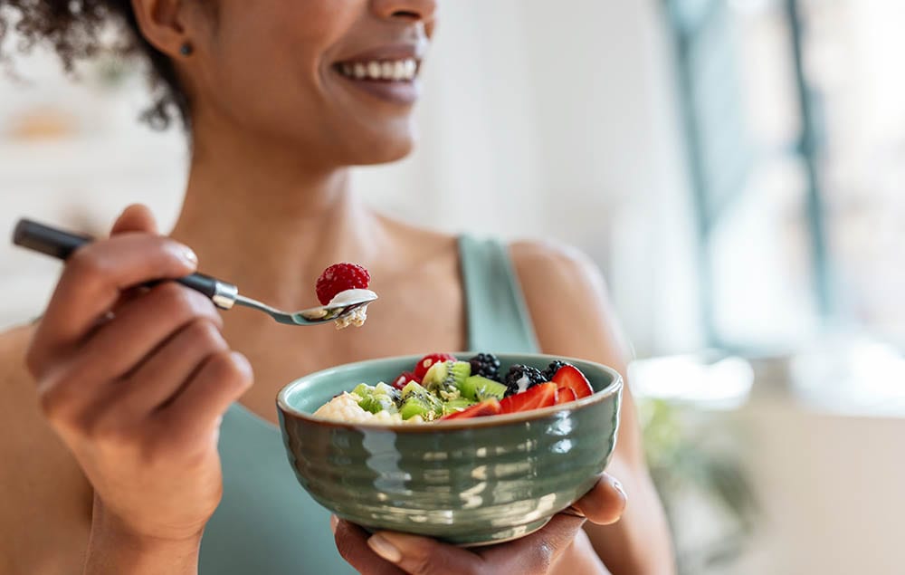 Woman eating a bowl of fresh fruit and oats as part of a chronic condition nutrition plan
