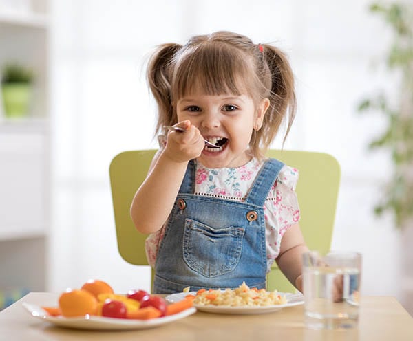 Young child happily eating a healthy meal of fruits and vegetables