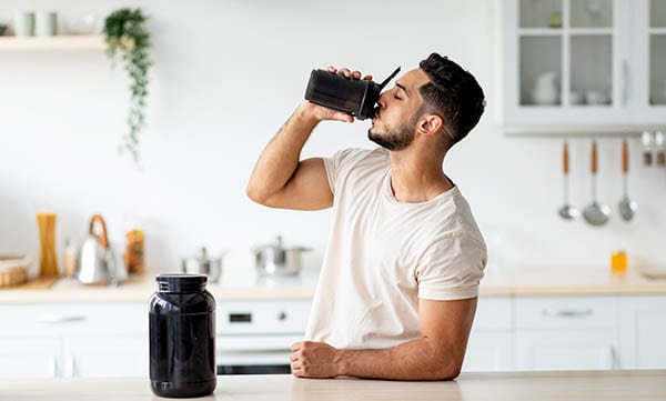 Man drinking a sports nutrition shake in the kitchen after training