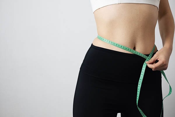 Woman measuring her waist with a tape measure to track weight management progress
